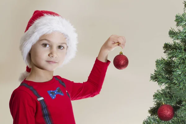 Niño pequeño en gorra de Santa con juguete de Navidad cerca del árbol de Navidad —  Fotos de Stock