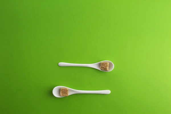 Two white spoons with brown sugar cubes on greenery background. Top view. Copy space for text. — Stock Photo, Image