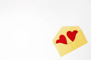Sarı zarf ve iki kırmızı kalp beyaz masa üzerinde hissetti. Üstten Görünüm. Kopya alanı.