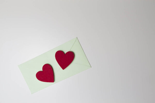 Зеленый конверт и два красных сердца на белом столе. Вид сверху
.