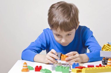 Oturma ve renkli plastik inşaat oyuncak blokları için masada seyir konsantre çocuk