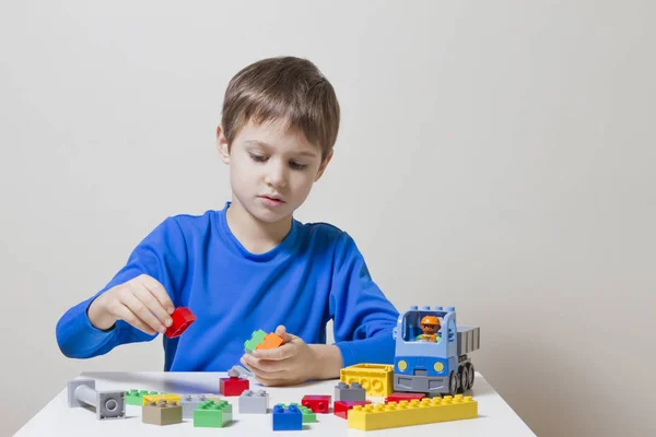 Criança concentrada sentada e olhando para blocos de brinquedos de construção de plástico colorido na mesa — Fotografia de Stock