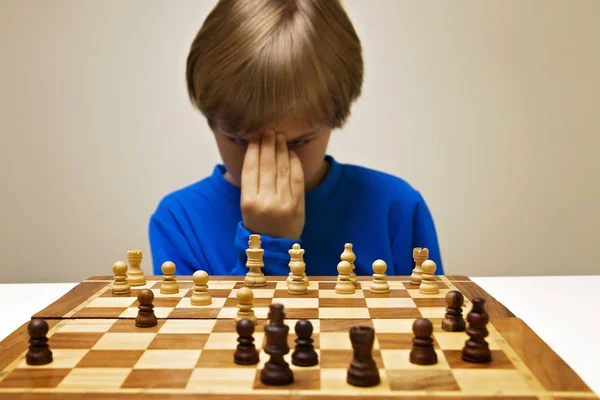 Серйозний розумний хлопчик дивиться на шахову дошку і думає про наступний хід — стокове фото