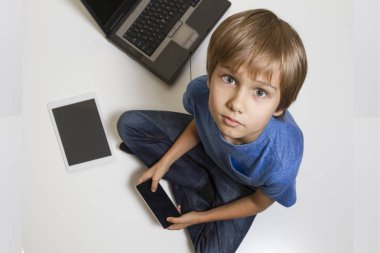 Cep telefonu katta oturan küçük bir çocuk. Dijital tablet, dizüstü bilgisayar, bilgisayar her yerde. Üstten Görünüm. Eğitim, teknoloji kavramı