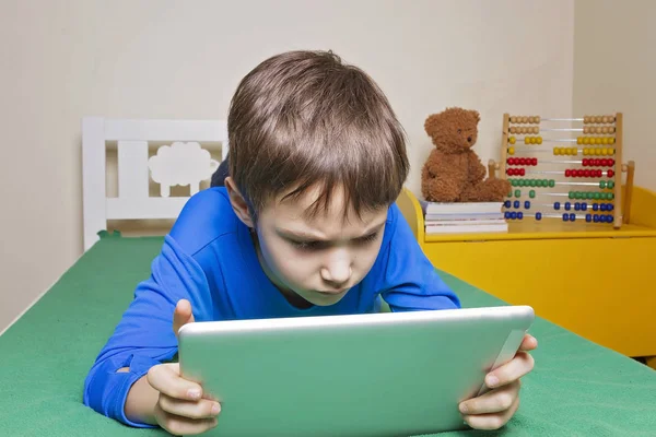 Concentrated child with digital tablet computer lying on the bed at home