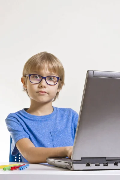 Menino com óculos usando computador portátil enquanto sentado na mesa em casa. Tecnologia, conceito de educação — Fotografia de Stock