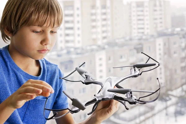 Un niño jugando con un dron. Chico cerca de la ventana sosteniendo el cuadrohelicóptero en su mano. Tecnología, concepto de juguetes de ocio — Foto de Stock