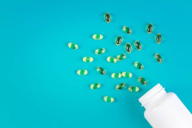 Omega 3 balık yağı kapsülleri mavi arka planda şişeden dökülüyor..