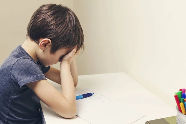 Kis gyerek gyártott otthon a házi feladatát. A fiú fáradt, és magában foglalja az arcát a kezével — Stock Fotó