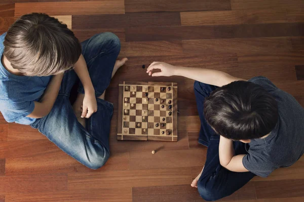 Kids playing chess sitting on wooden floor. Top view. Game, education, lifestyle, leisure concept — Stock Photo, Image