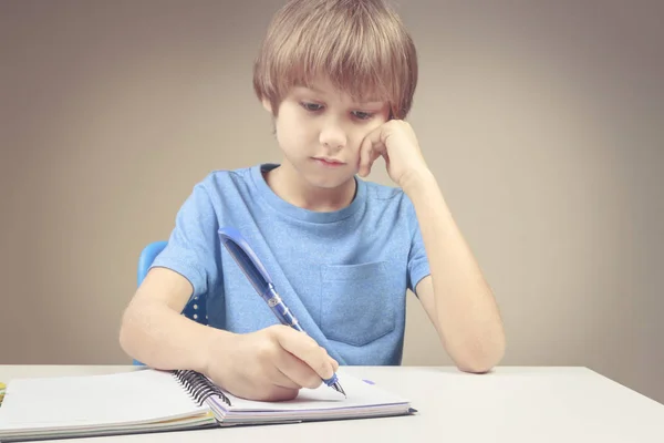 Um rapaz a escrever num bloco de notas. Rapaz a fazer os seus exercícios de casa — Fotografia de Stock