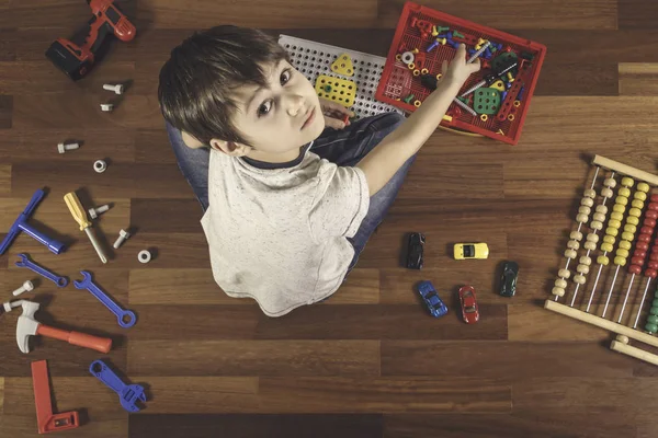Bambino che gioca con i giocattoli mentre è seduto sul pavimento in legno nella sua camera.Vista dall'alto — Foto Stock