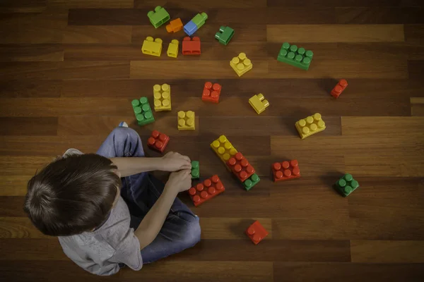 Child sitting on the wooden floor and playing with colorful plastic blocks. Top view — Stock Photo, Image