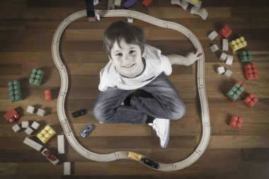 Oyuncak tren ile mutlu bir çocuk. Kamera ve gülümseyen bakarak ahşap zemin karınca oturan çocuk. Üstten Görünüm