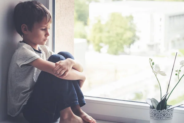 Niño triste sentado en el escudo de la ventana . — Foto de Stock