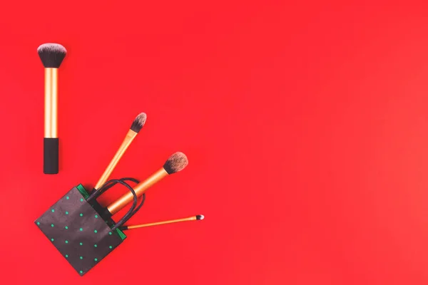 Maquillaje cepillos con bolsa de compras de papel blanco sobre fondo rojo — Foto de Stock