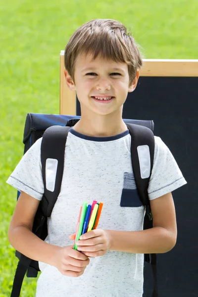 Joyeux écolier avec stylos et sac à dos contre le tableau noir. Éducation, concept de retour à l'école — Photo