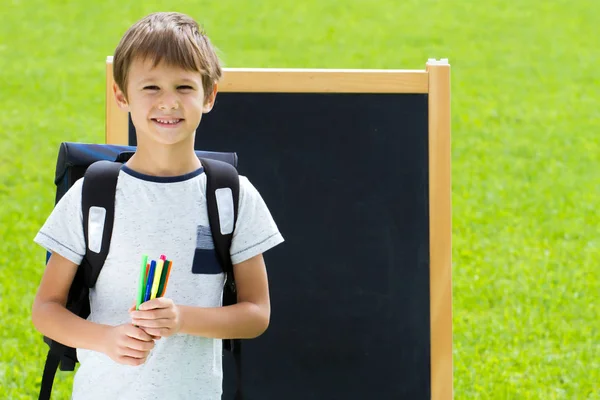 Lycklig skolpojke med pennor och ryggsäck mot tavlan. Utbildning, tillbaka till skolan-konceptet — Stockfoto