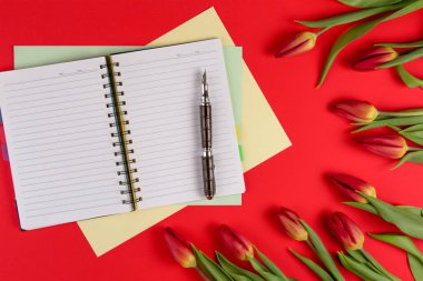 Açık kağıt defter ve kalem kırmızı zemin üzerine kırmızı bahar lale çiçekleri ile.