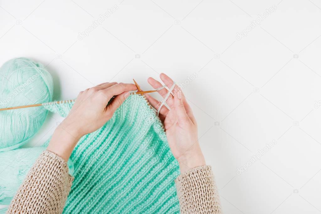 Top view of a woman hands knitting with wooden needles on white background