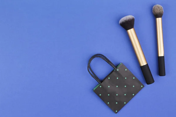 Make up brushes with black polka dot paper shopping bag on blue background — Stock Photo, Image