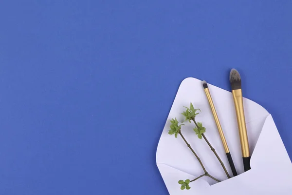 Componen los pinceles en el sobre blanco con la primera primavera por las hojas tiernas y los brotes en las ramitas de los árboles . — Foto de Stock