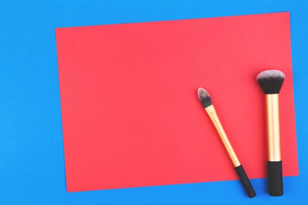 Maquillaje de pinceles con papel rojo en blanco sobre fondo azul — Foto de Stock