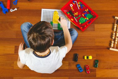 Kattaki odasında otururken oyuncaklar araç kiti ile oynayan çocuk. Üstten Görünüm