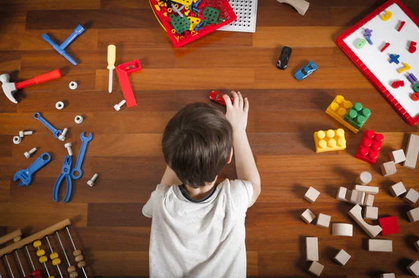 Vista superior del niño pequeño acostado en el suelo de madera y jugando con juguetes de colores . — Foto de Stock