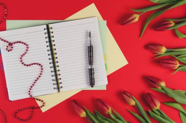 Açık kağıt defter ve kalem kırmızı zemin üzerine kırmızı bahar lale çiçekleri ile.