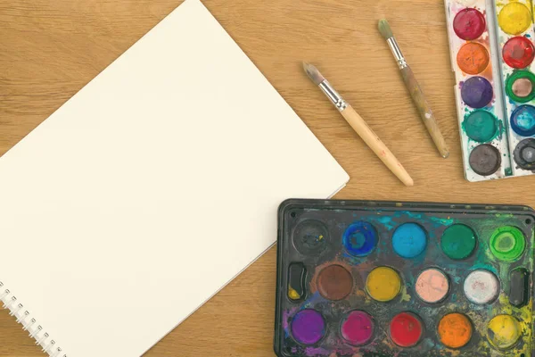 Pinturas de acuarela, pinceles para pintar y hoja de papel blanco en blanco sobre fondo de madera . —  Fotos de Stock