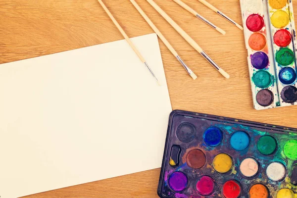 Pinturas de acuarela, pinceles para pintar y hoja de papel blanco en blanco sobre fondo de madera . —  Fotos de Stock