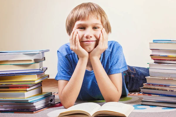 Rapaz sorridente entre as pilhas de livros . — Fotografia de Stock