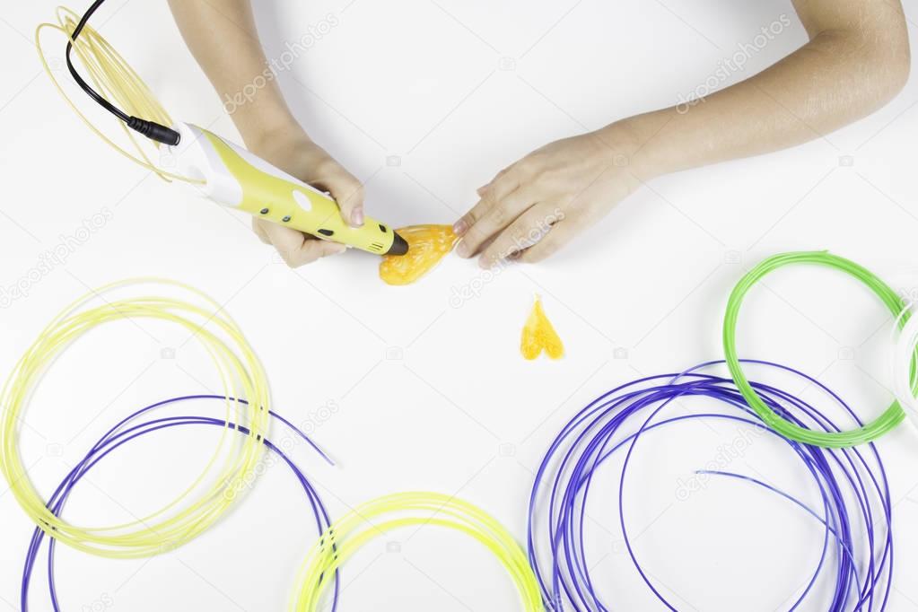 Kids hand holding yellow 3D printing pen with filaments and makes heart..