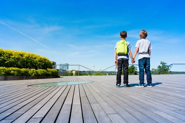 Vista posteriore di due ragazzi caucasici che si tengono per mano e guardano la città — Foto Stock