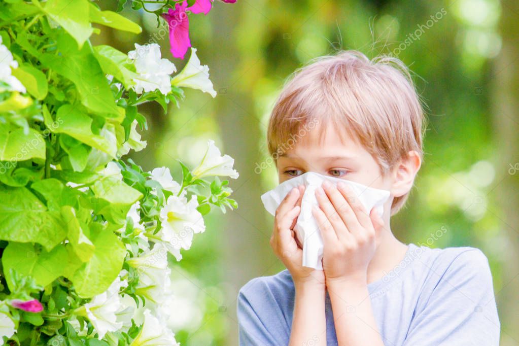 Allergy. Little boy is blowing his nose near tree in bloom.