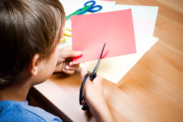 Criança cortando papel colorido com tesoura na mesa — Fotografia de Stock