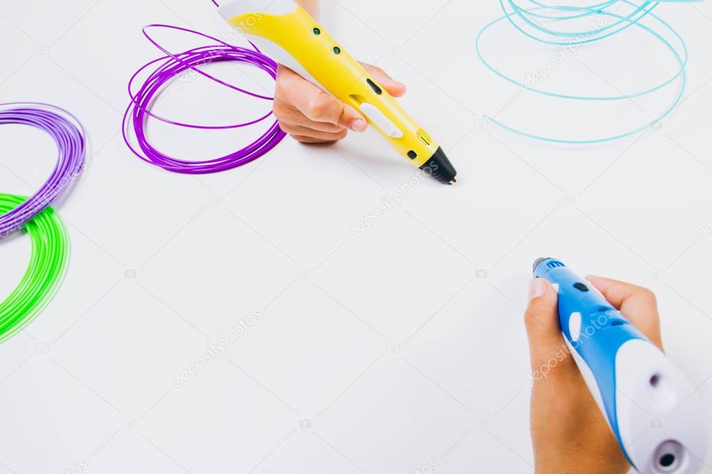 Kids hands holding 3d printing pens with filaments on white background. Top view