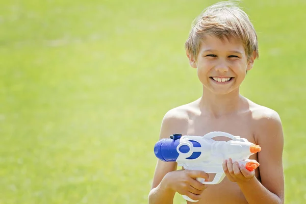Lächelnder Junge spielt an Sommertagen mit Wasserpistole — Stockfoto