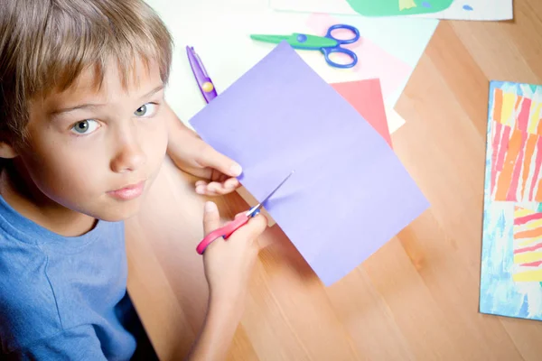 Bambino che taglia carta colorata con le forbici a tavola — Foto Stock