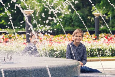 Happy kids playing near fountain in the city park clipart