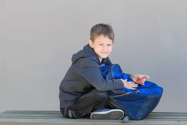 Pojke med ryggsäck som sitter på bänken efter skolan — Stockfoto