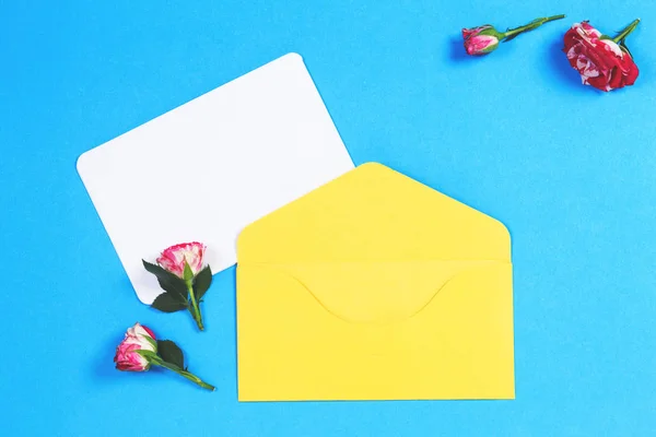 Κενό ευχετήρια κάρτα με κίτρινο φάκελο και ροζ τριαντάφυλλο λουλούδια σε μπλε φόντο — Φωτογραφία Αρχείου