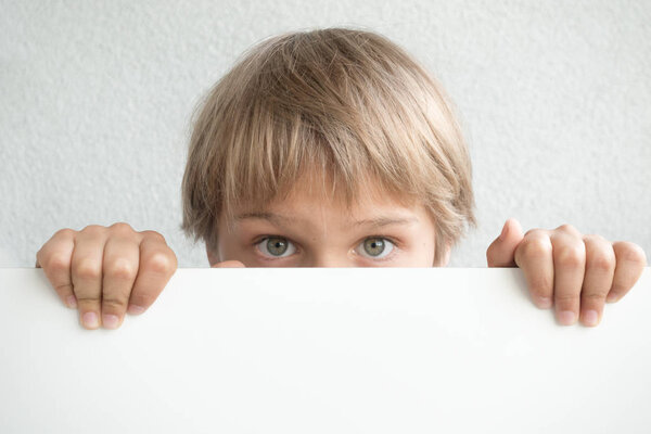 Little boy holding blank white sign or placard hiding his face