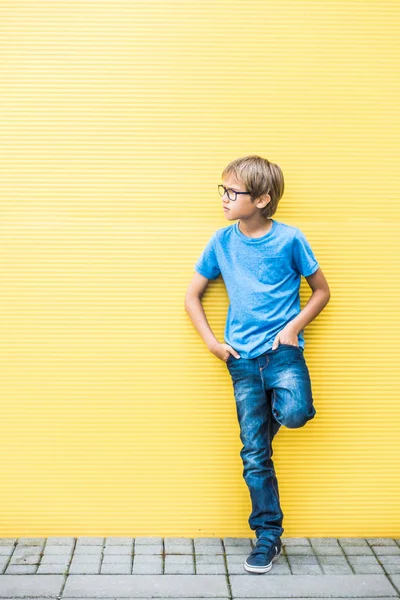 Menino com óculos de pé perto da parede amarela oudoors — Fotografia de Stock