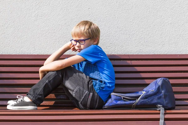 Niño triste y cansado sentado solo en el banco al aire libre . — Foto de Stock