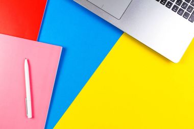 Mavi ve sarı renk arka plan üzerinde dizüstü bilgisayar, kağıt defter ve beyaz kalem Üstten Görünüm