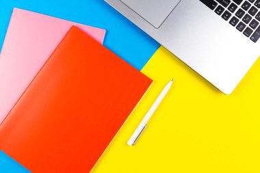 Mavi ve sarı renk arka plan üzerinde dizüstü bilgisayar, kağıt defter ve beyaz kalem Üstten Görünüm