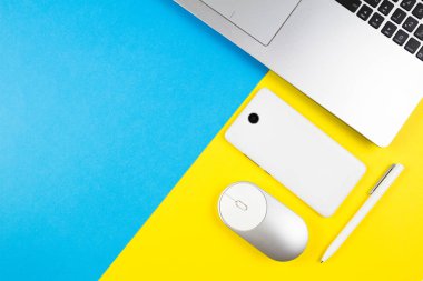 Dizüstü bilgisayar, bilgisayar faresi, cep telefonu ve mavi ve sarı renk arka plan üzerinde beyaz kalem ile modern çalışma alanı