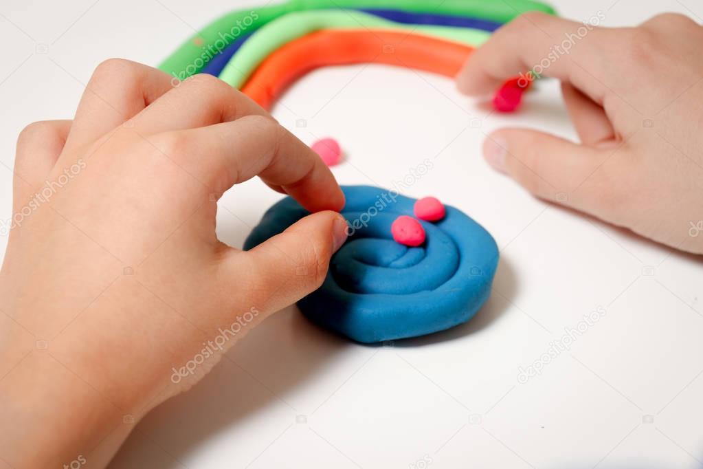 Child hands molding modeling clay or plasticine on white table